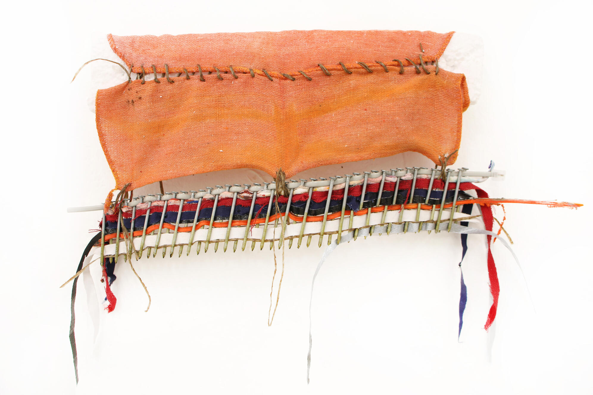 &quot;Weaving on Nails&quot;, 2024, shop rag, styrofoam, sinew, metal, traffic cone, uniform, found objects, 6&quot; × 18&quot;.
