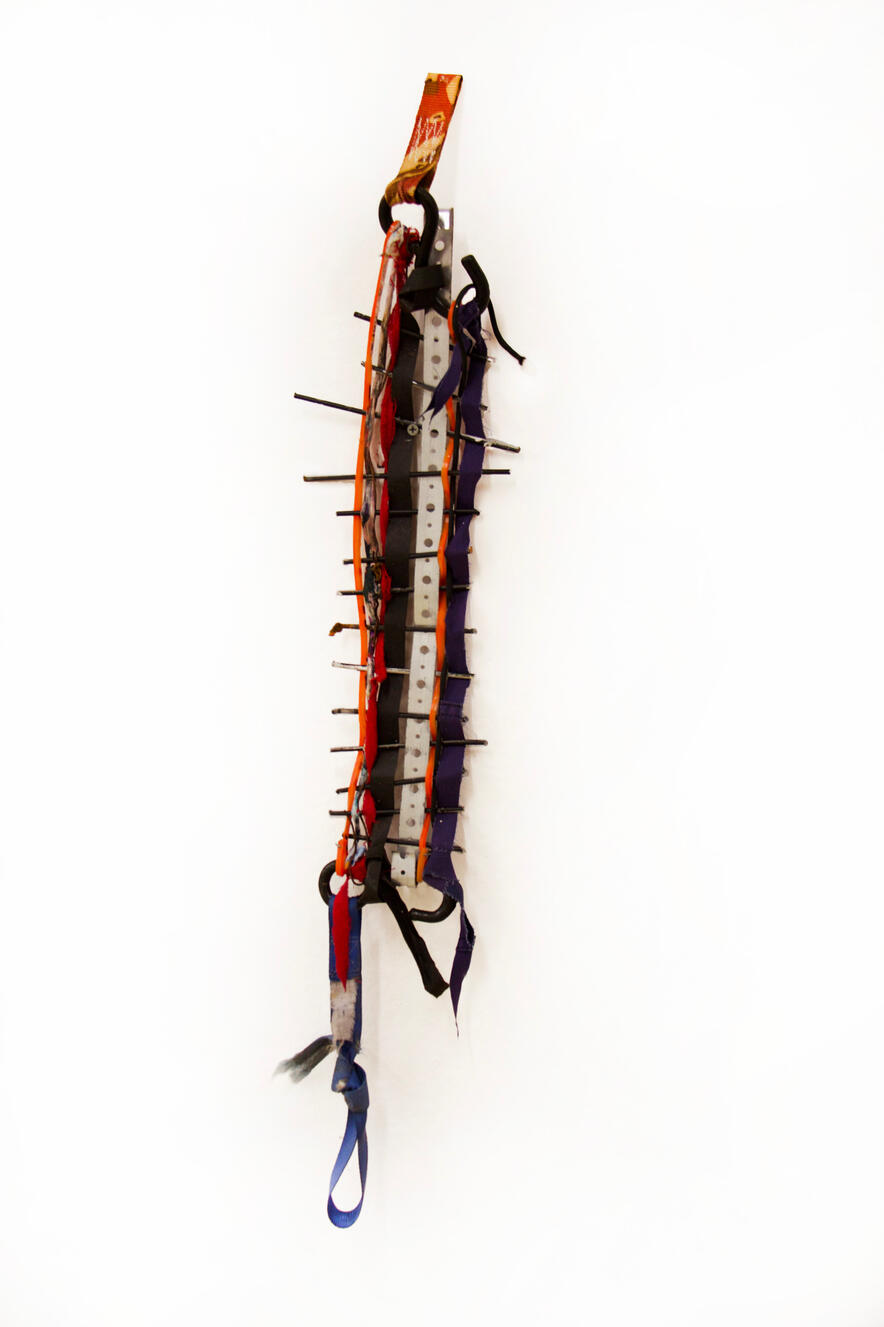 "Weaving on Wire and Straps", 2024, shop rag, sinew, metal, traffic cone, uniform, found objects, 6" × 18".